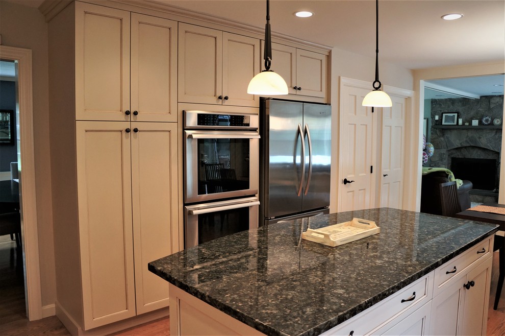 Example of a mid-sized transitional l-shaped medium tone wood floor and brown floor open concept kitchen design in Boston with an undermount sink, recessed-panel cabinets, beige cabinets, granite countertops, beige backsplash, subway tile backsplash, stainless steel appliances, an island and black countertops