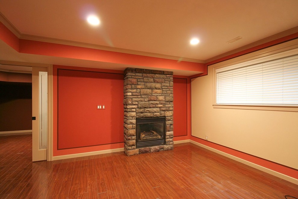 Inspiration for a mid-sized transitional underground medium tone wood floor and brown floor basement remodel in Vancouver with orange walls, a standard fireplace and a stone fireplace