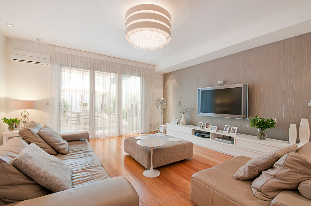 Photo of an expansive contemporary open concept living room in Melbourne with beige walls, medium hardwood floors, no fireplace and a wall-mounted tv.
