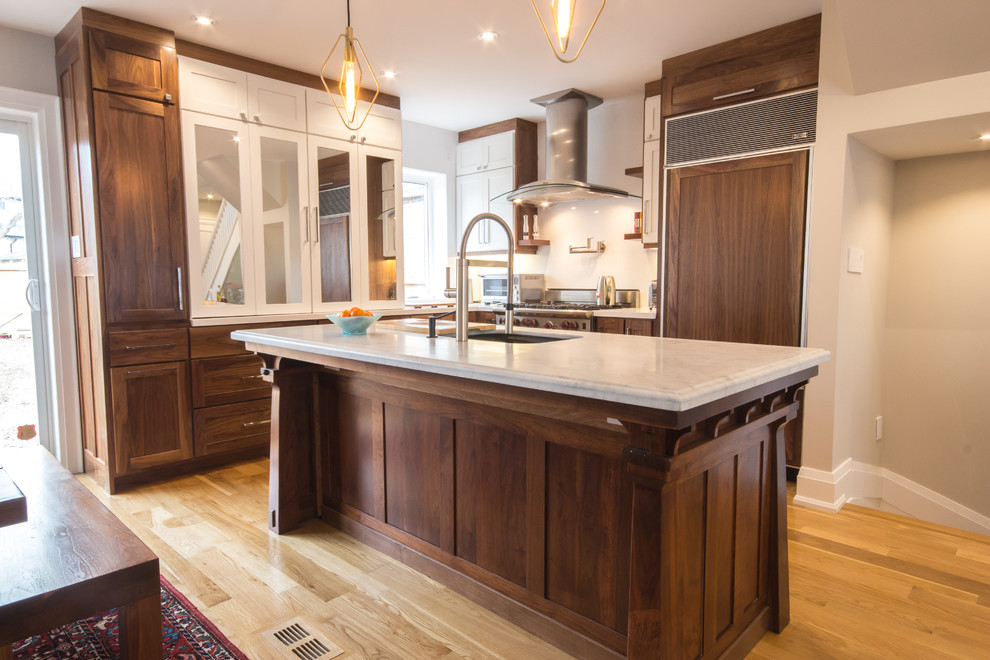This is an example of a mid-sized transitional l-shaped open plan kitchen in Toronto with an undermount sink, shaker cabinets, medium wood cabinets, quartzite benchtops, white splashback, panelled appliances, light hardwood floors, with island and brown floor.