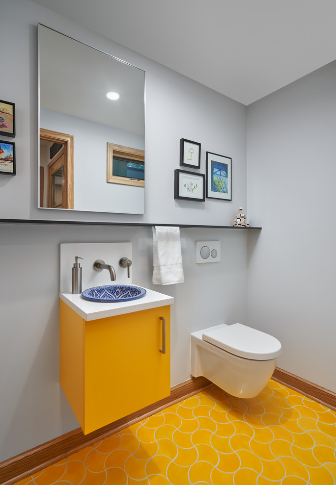 This is an example of a contemporary powder room in Minneapolis with flat-panel cabinets, yellow cabinets, a wall-mount toilet, grey walls, a drop-in sink, yellow floor and white benchtops.