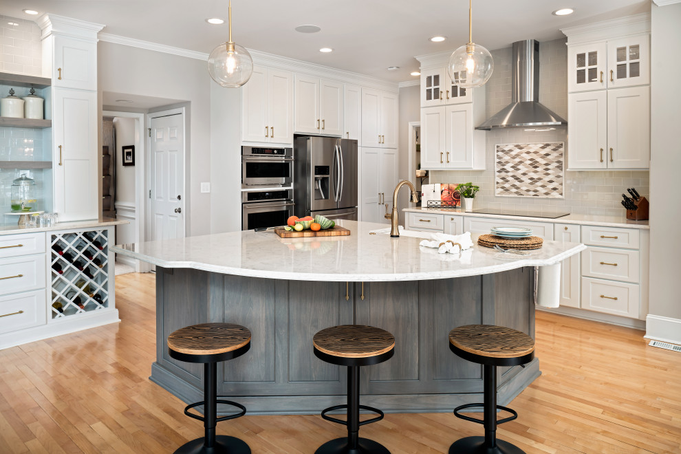 Inspiration for a mid-sized coastal l-shaped light wood floor and yellow floor open concept kitchen remodel in Charlotte with a farmhouse sink, recessed-panel cabinets, white cabinets, quartz countertops, gray backsplash, ceramic backsplash, stainless steel appliances, an island and white countertops