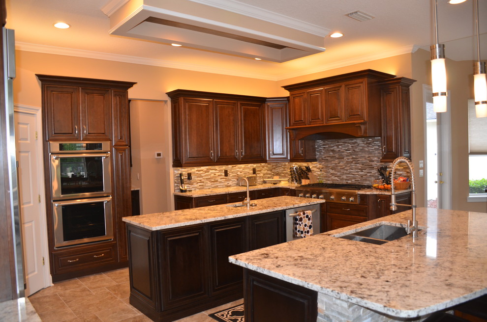 This is an example of a large eclectic u-shaped separate kitchen in Jacksonville with an undermount sink, raised-panel cabinets, dark wood cabinets, granite benchtops, metallic splashback, matchstick tile splashback, stainless steel appliances, porcelain floors and multiple islands.