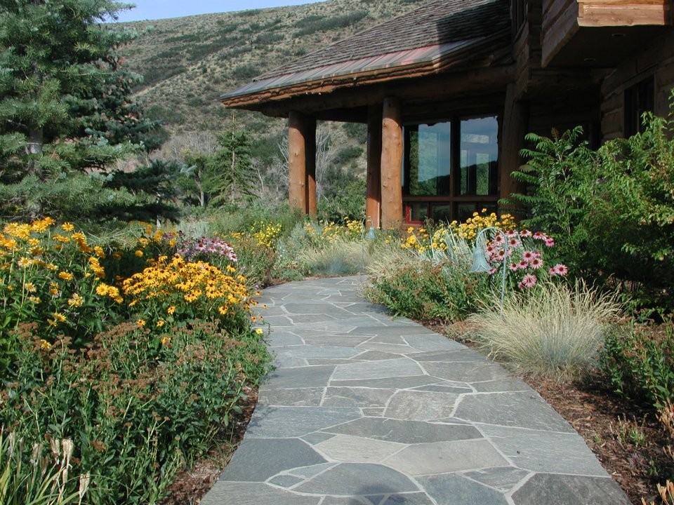 This is an example of a mid-sized country front yard full sun garden for summer in Salt Lake City with a garden path and natural stone pavers.