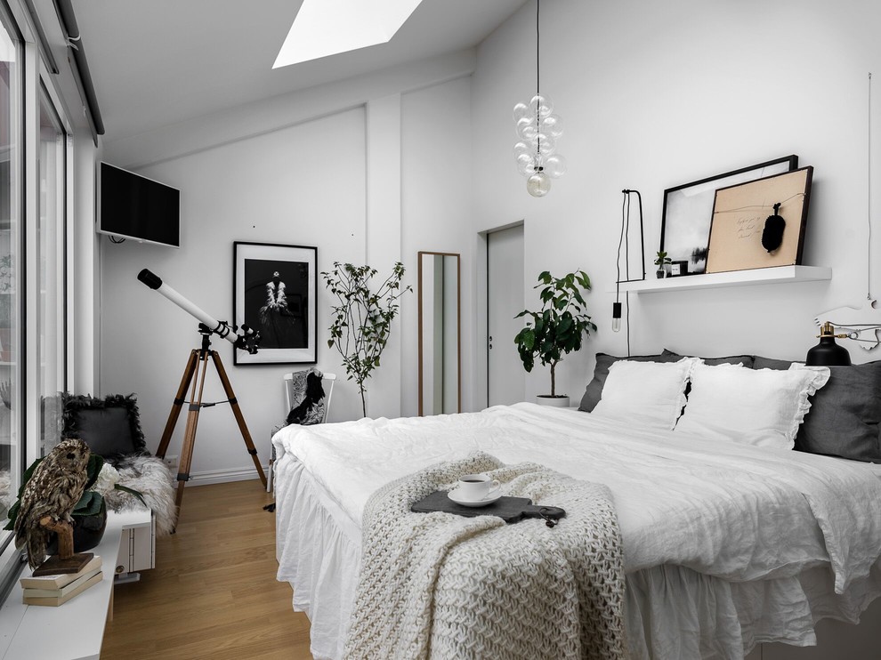 This is an example of a large scandinavian master bedroom in Stockholm with white walls and light hardwood floors.