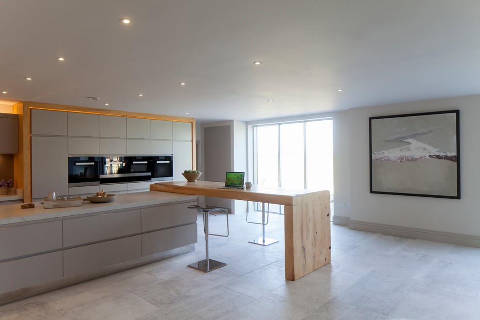 Inspiration for an expansive contemporary open plan kitchen in Cheshire with a double-bowl sink, flat-panel cabinets, grey cabinets, quartzite benchtops, grey splashback, glass sheet splashback, stainless steel appliances, porcelain floors and multiple islands.