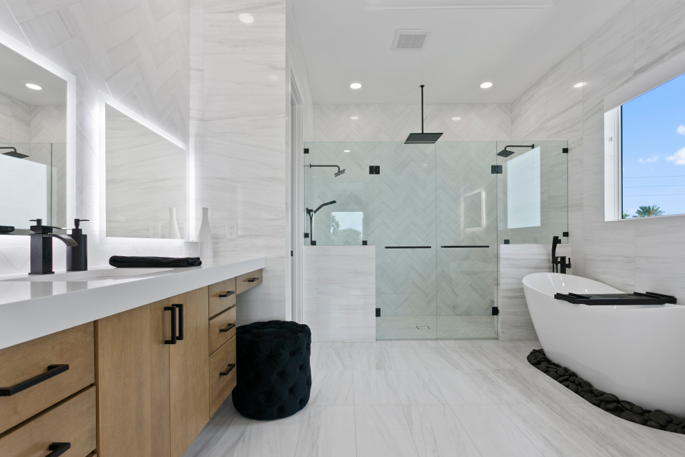 На фото: большая главная ванная комната, совмещенная с туалетом в современном стиле с фасадами разных видов, серыми фасадами, отдельно стоящей ванной, душем без бортиков, белой плиткой, каменной плиткой, белыми стенами, мраморным полом, врезной раковиной, столешницей из кварцита, белым полом, душем с распашными дверями, белой столешницей, сиденьем для душа, тумбой под две раковины, подвесной тумбой, любым потолком и любой отделкой стен