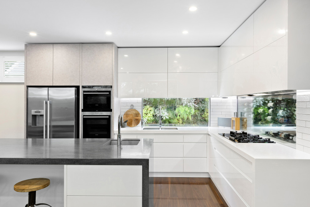 This is an example of a mid-sized contemporary l-shaped kitchen in Melbourne with an undermount sink, flat-panel cabinets, white cabinets, window splashback, with island, brown floor and white benchtop.