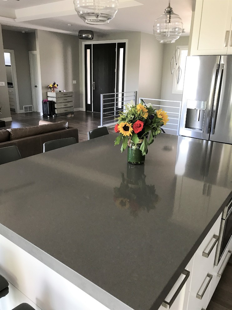 Mid-sized transitional l-shaped light wood floor and gray floor eat-in kitchen photo with an undermount sink, recessed-panel cabinets, white cabinets, quartz countertops, gray backsplash, ceramic backsplash, stainless steel appliances and an island