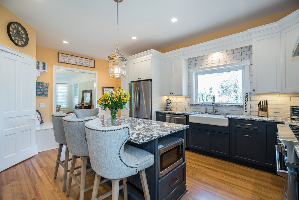 This is an example of a large traditional l-shaped eat-in kitchen in New York with subway tile splashback, stainless steel appliances, with island, a farmhouse sink, shaker cabinets, white cabinets, quartz benchtops, light hardwood floors and blue benchtop.