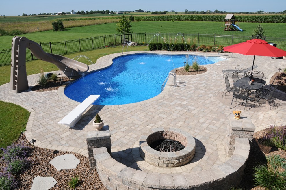 Large traditional backyard custom-shaped pool in Chicago with a water slide and concrete pavers.