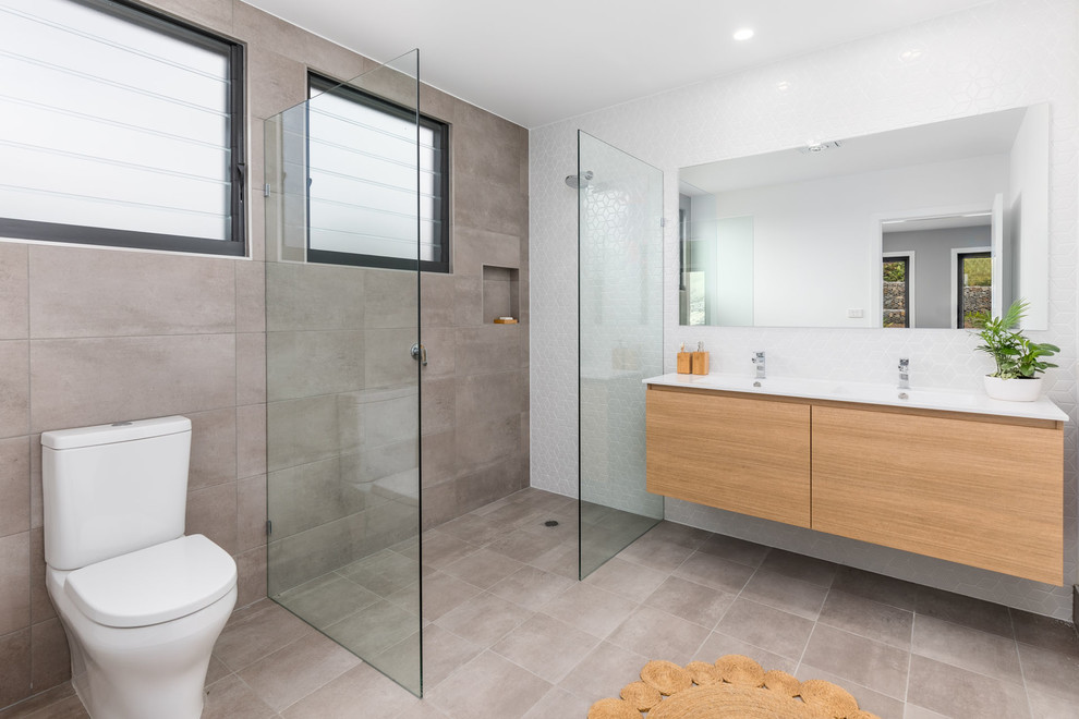 Photo of a 3/4 wet room bathroom in Other with flat-panel cabinets, medium wood cabinets, a two-piece toilet, beige tile, white tile, an integrated sink, beige floor, an open shower and white benchtops.