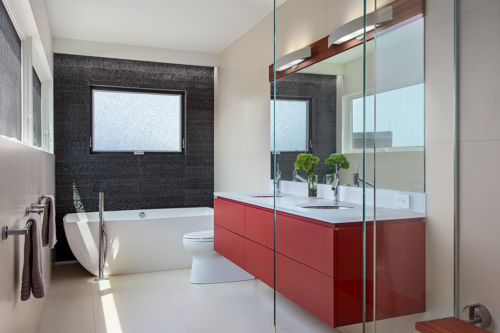 Photo of a mid-sized contemporary master bathroom in Bridgeport with an undermount sink, flat-panel cabinets, red cabinets, a freestanding tub, a one-piece toilet, gray tile, stone tile, beige walls, porcelain floors, a corner shower, quartzite benchtops, beige floor and a hinged shower door.