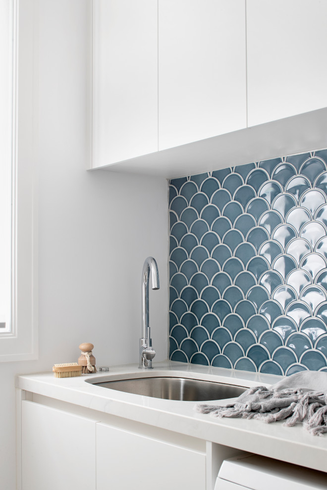 Mid-sized contemporary galley dedicated laundry room in Melbourne with an undermount sink, flat-panel cabinets, white cabinets, quartz benchtops, blue splashback, ceramic splashback, ceramic floors, a side-by-side washer and dryer, grey floor and white benchtop.