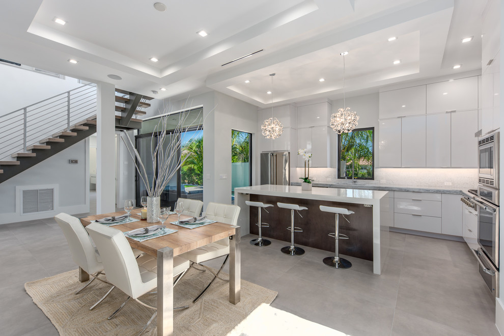 This is an example of a beach style l-shaped open plan kitchen in Miami with an undermount sink, flat-panel cabinets, white cabinets, grey splashback, with island, grey floor and grey benchtop.