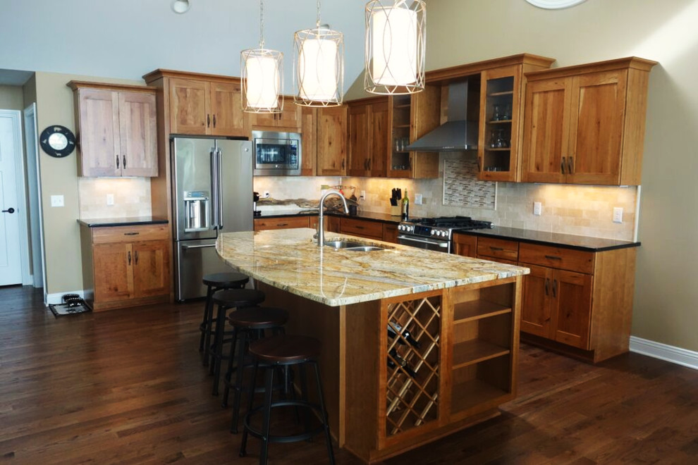 Inspiration for a rustic l-shaped dark wood floor eat-in kitchen remodel with an undermount sink, recessed-panel cabinets, medium tone wood cabinets, granite countertops, beige backsplash, stone tile backsplash, stainless steel appliances and an island