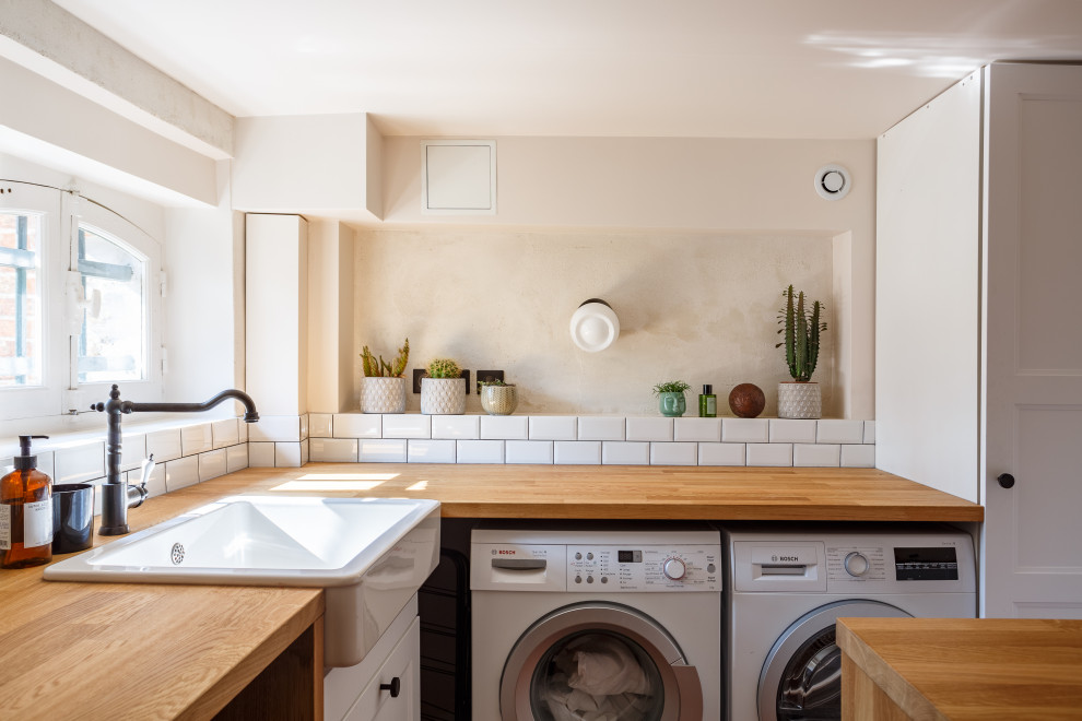 This is an example of a mid-sized mediterranean u-shaped dedicated laundry room in Paris with a farmhouse sink, white cabinets, wood benchtops, white splashback, subway tile splashback, white walls, terra-cotta floors and red floor.