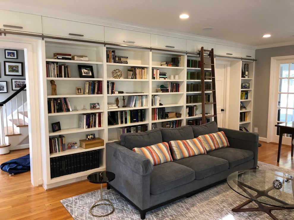 Design ideas for a large transitional enclosed family room in Raleigh with a library, white walls, light hardwood floors, no fireplace, a concealed tv and brown floor.