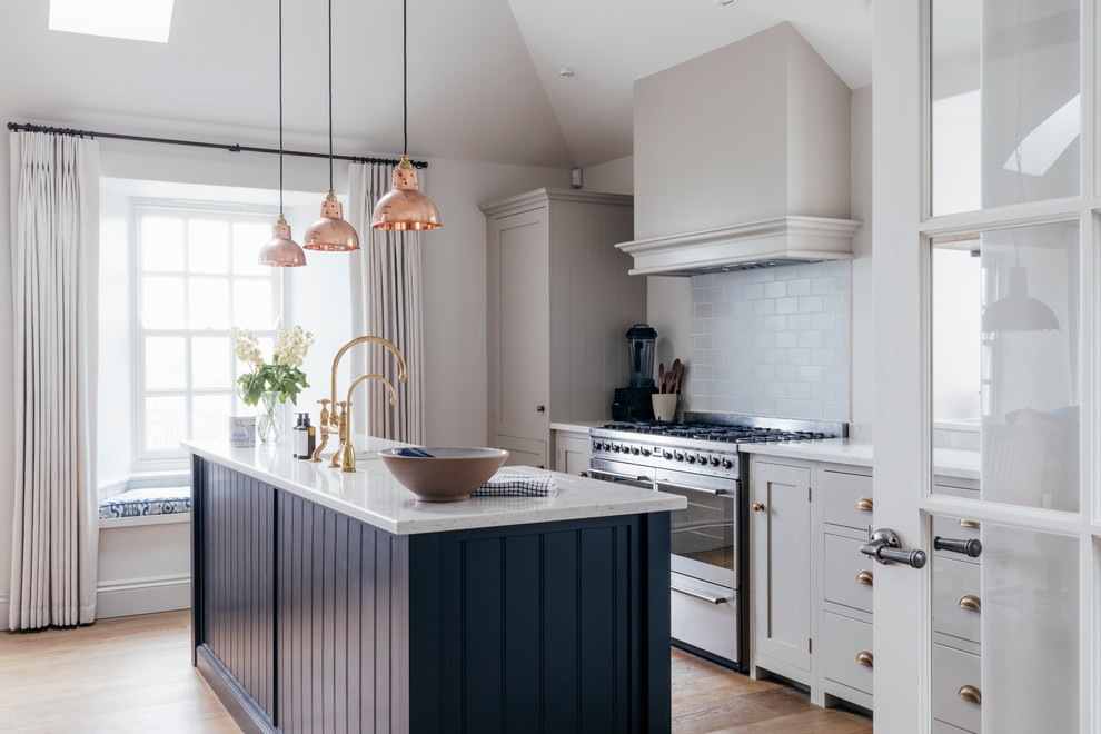 Mid-sized beach style galley kitchen in Cornwall with a farmhouse sink, grey cabinets, solid surface benchtops, blue splashback, ceramic splashback, stainless steel appliances, medium hardwood floors, with island, brown floor and white benchtop.