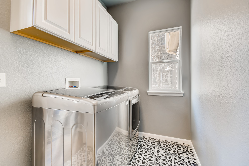 Small contemporary single-wall utility room in Denver with raised-panel cabinets, white cabinets, grey walls and a side by side washer and dryer.