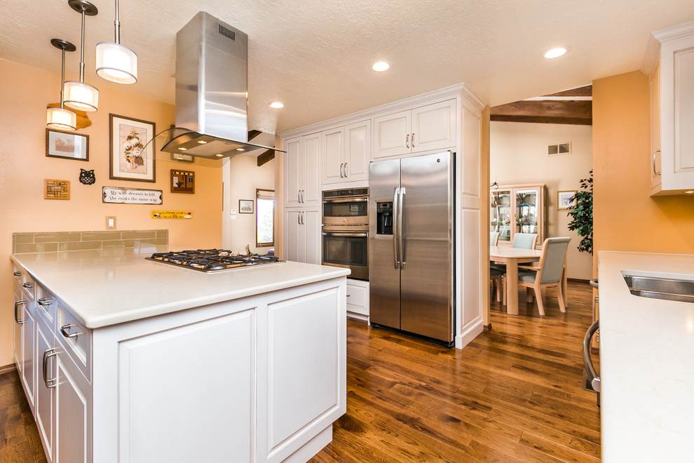 Inspiration for a mid-sized transitional u-shaped medium tone wood floor enclosed kitchen remodel in Albuquerque with a double-bowl sink, raised-panel cabinets, white cabinets, quartz countertops, beige backsplash, subway tile backsplash, stainless steel appliances and an island
