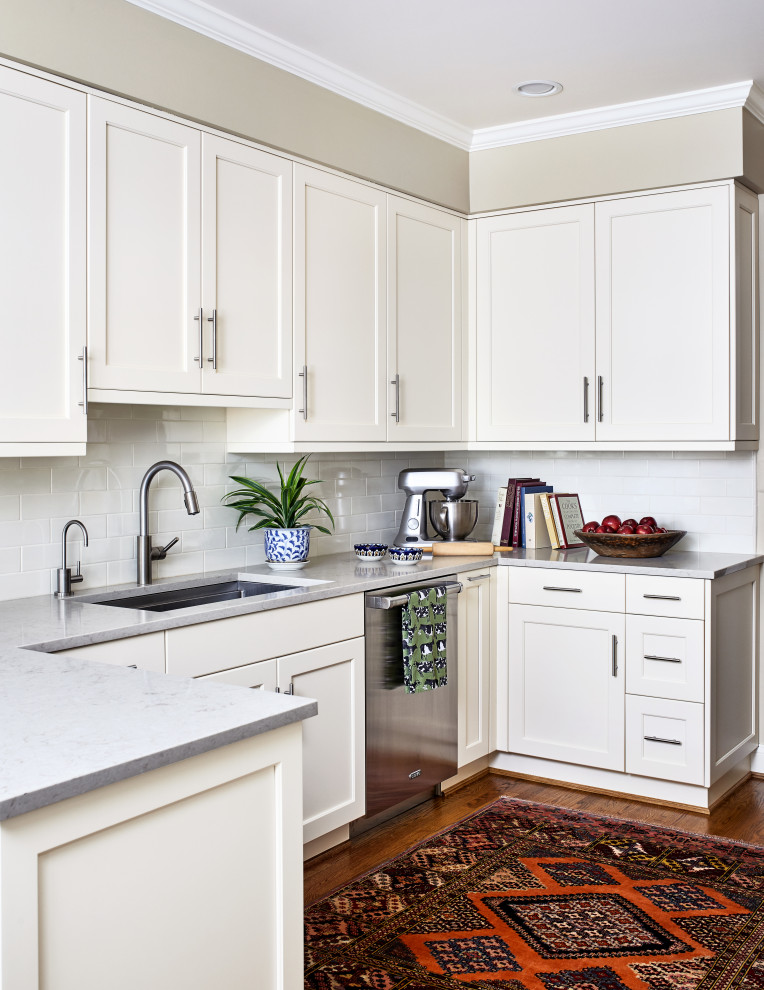 This is an example of a mid-sized transitional u-shaped separate kitchen in DC Metro with an undermount sink, shaker cabinets, white cabinets, quartzite benchtops, white splashback, subway tile splashback, stainless steel appliances, medium hardwood floors, a peninsula, brown floor and grey benchtop.