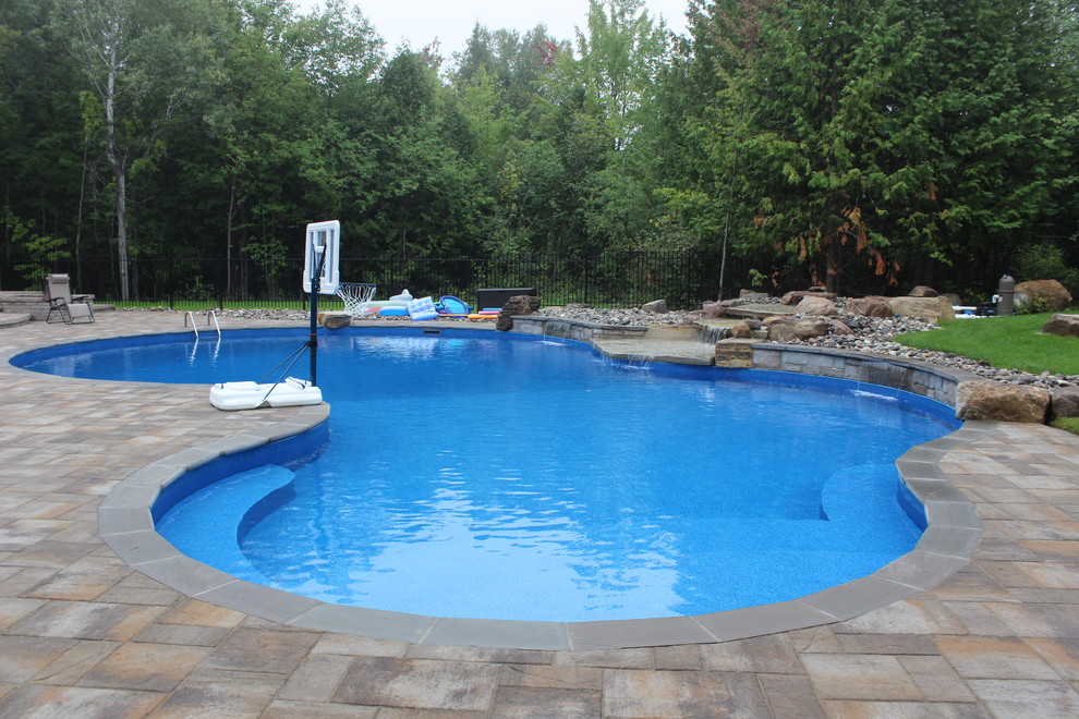 Photo of a large contemporary backyard kidney-shaped natural pool in Ottawa with a water feature and stamped concrete.