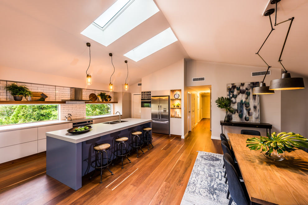 Large industrial galley eat-in kitchen in Sydney with an undermount sink, quartz benchtops, white splashback, stainless steel appliances, porcelain floors, with island, orange floor, flat-panel cabinets, beige cabinets and subway tile splashback.