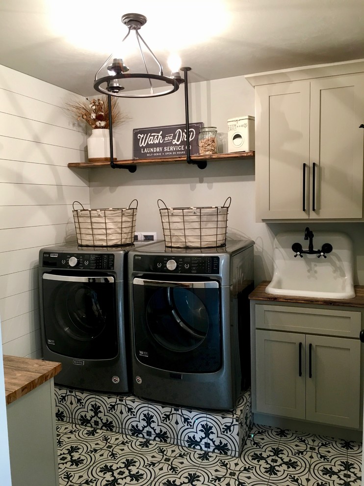 Mid-sized country galley dedicated laundry room in Other with shaker cabinets, beige cabinets, wood benchtops, grey walls, ceramic floors, a side-by-side washer and dryer, black floor and a drop-in sink.
