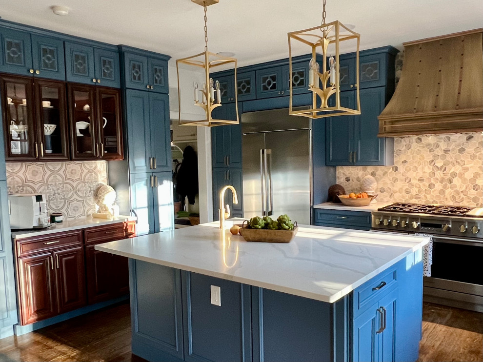 This is an example of a large contemporary u-shaped kitchen/diner in Philadelphia with a belfast sink, beaded cabinets, brown cabinets, engineered stone countertops, blue splashback, cement tile splashback, stainless steel appliances, medium hardwood flooring, an island and white worktops.