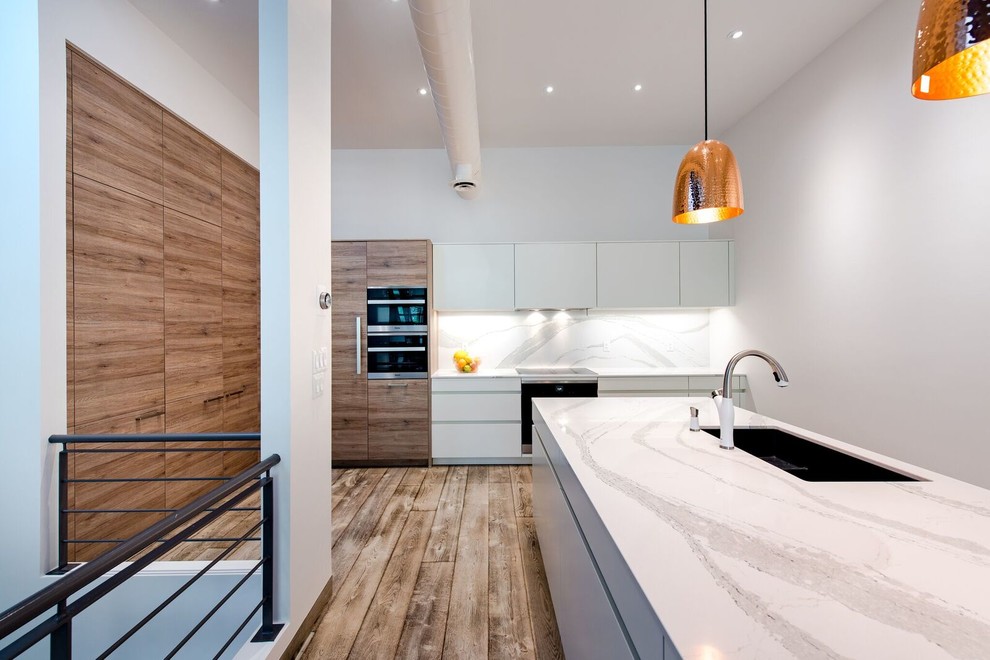 Inspiration for a mid-sized transitional galley medium tone wood floor eat-in kitchen remodel in Toronto with an undermount sink, flat-panel cabinets, medium tone wood cabinets, quartz countertops, white backsplash, stainless steel appliances and an island