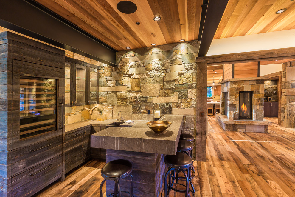 Inspiration for a mid-sized country u-shaped seated home bar in Sacramento with an undermount sink, flat-panel cabinets, medium wood cabinets, stone tile splashback and light hardwood floors.
