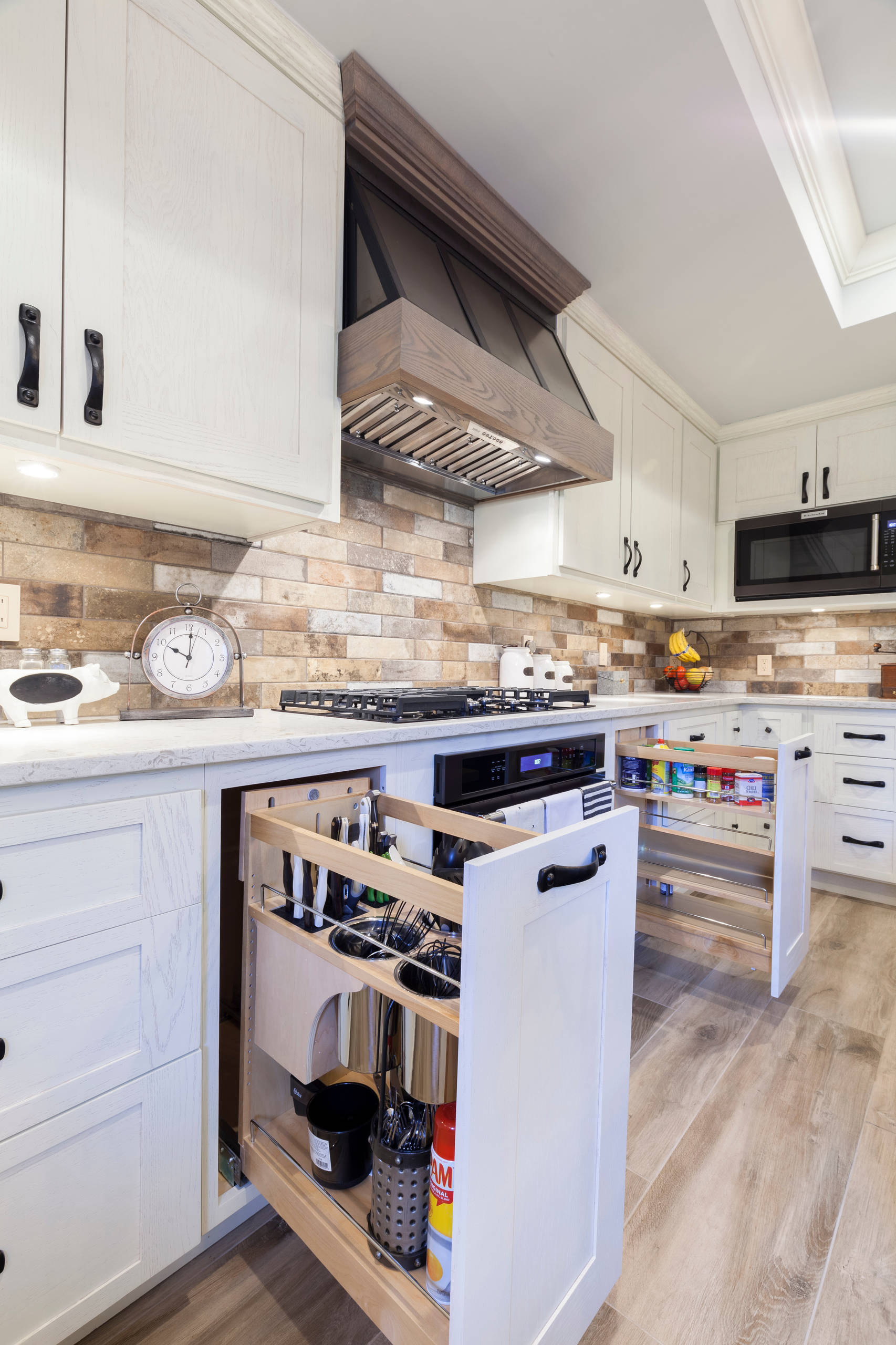 Farmhouse kitchen with a stone farmhouse apron sink, black kitchenaid dishwasher, fridge, stovetop, oven, microwave, and custom farmhouse table, white shaker cabinets. Pull out utensil and spice cabin