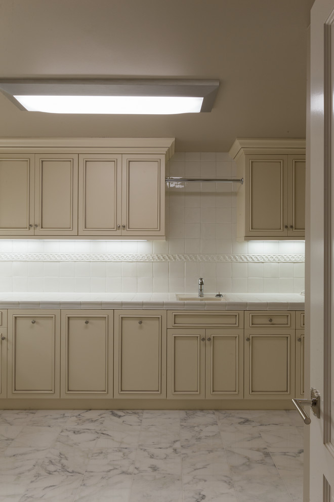 Design ideas for a large contemporary u-shaped utility room in San Francisco with an utility sink, raised-panel cabinets, white cabinets, tile benchtops, beige walls, marble floors and a side-by-side washer and dryer.