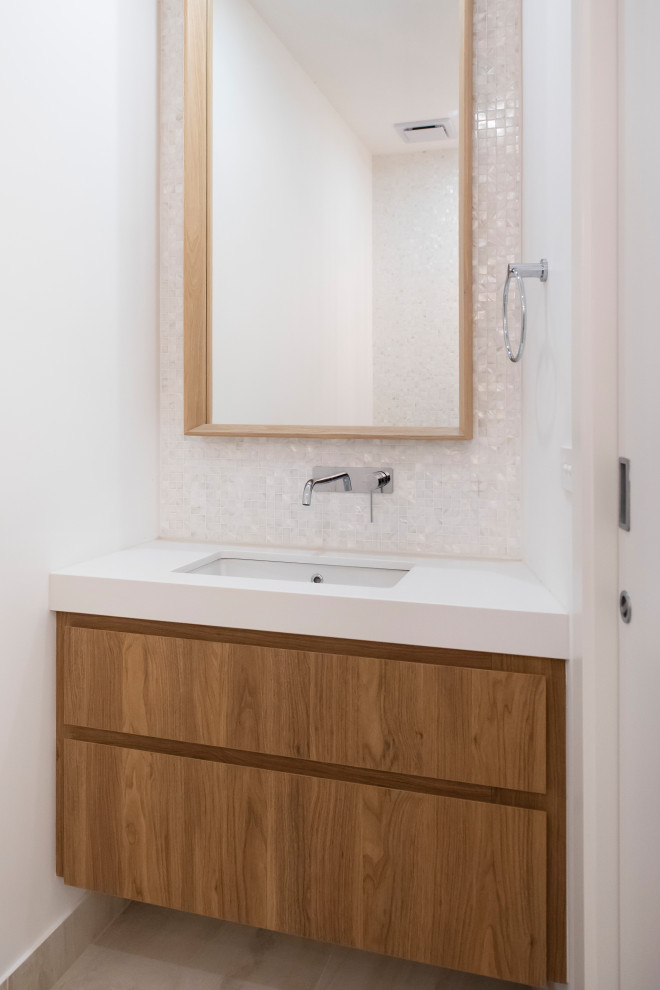 Design ideas for an expansive beach style powder room in Melbourne with raised-panel cabinets, medium wood cabinets, a one-piece toilet, multi-coloured tile, mosaic tile, white walls, porcelain floors, an undermount sink, engineered quartz benchtops, beige floor and white benchtops.