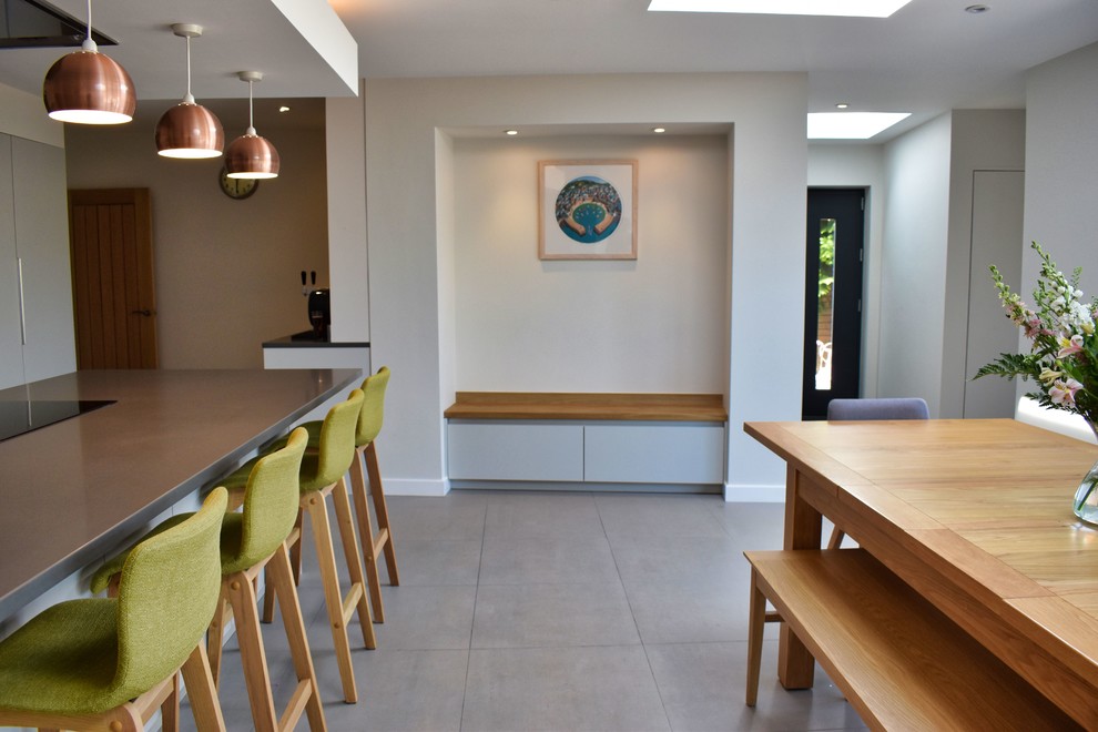 Large contemporary single-wall eat-in kitchen in Cambridgeshire with an undermount sink, flat-panel cabinets, grey cabinets, quartzite benchtops, brown splashback, glass tile splashback, black appliances, ceramic floors, a peninsula, grey floor and grey benchtop.