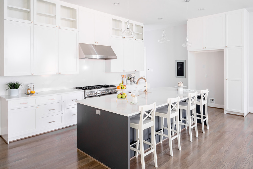 Example of a transitional single-wall medium tone wood floor and brown floor open concept kitchen design in Houston with a farmhouse sink, shaker cabinets, white cabinets, quartzite countertops, white backsplash, porcelain backsplash, stainless steel appliances, an island and white countertops