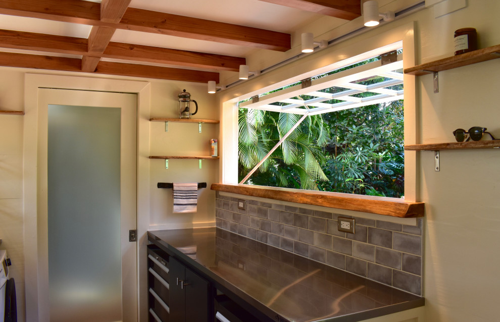 Small beach style u-shaped eat-in kitchen in Hawaii with a double-bowl sink, flat-panel cabinets, black cabinets, stainless steel benchtops, grey splashback, ceramic splashback, stainless steel appliances, laminate floors, with island, brown floor and grey benchtop.