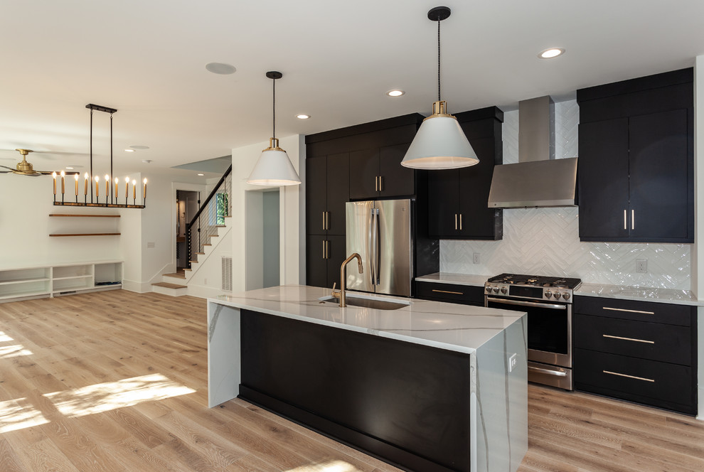 Mid-sized modern l-shaped open plan kitchen in Charleston with flat-panel cabinets, black cabinets, quartz benchtops, white splashback, subway tile splashback, stainless steel appliances, light hardwood floors, with island, white benchtop, an undermount sink and brown floor.