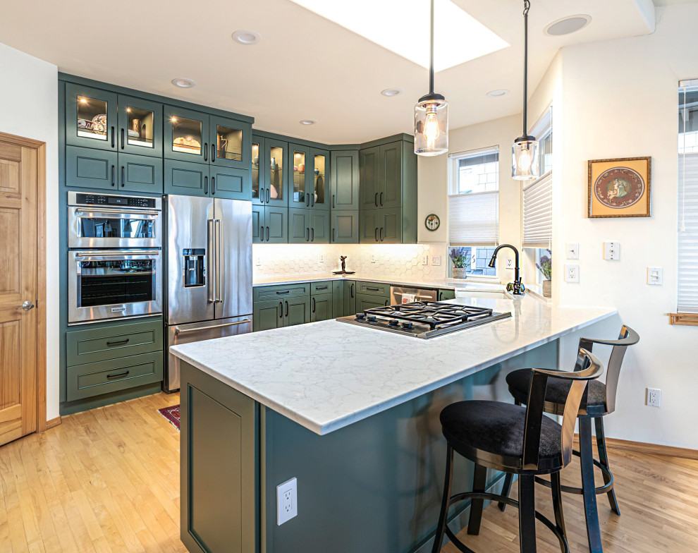 Example of a transitional u-shaped light wood floor and beige floor kitchen design in Seattle with a farmhouse sink, recessed-panel cabinets, green cabinets, white backsplash, stainless steel appliances, a peninsula and white countertops