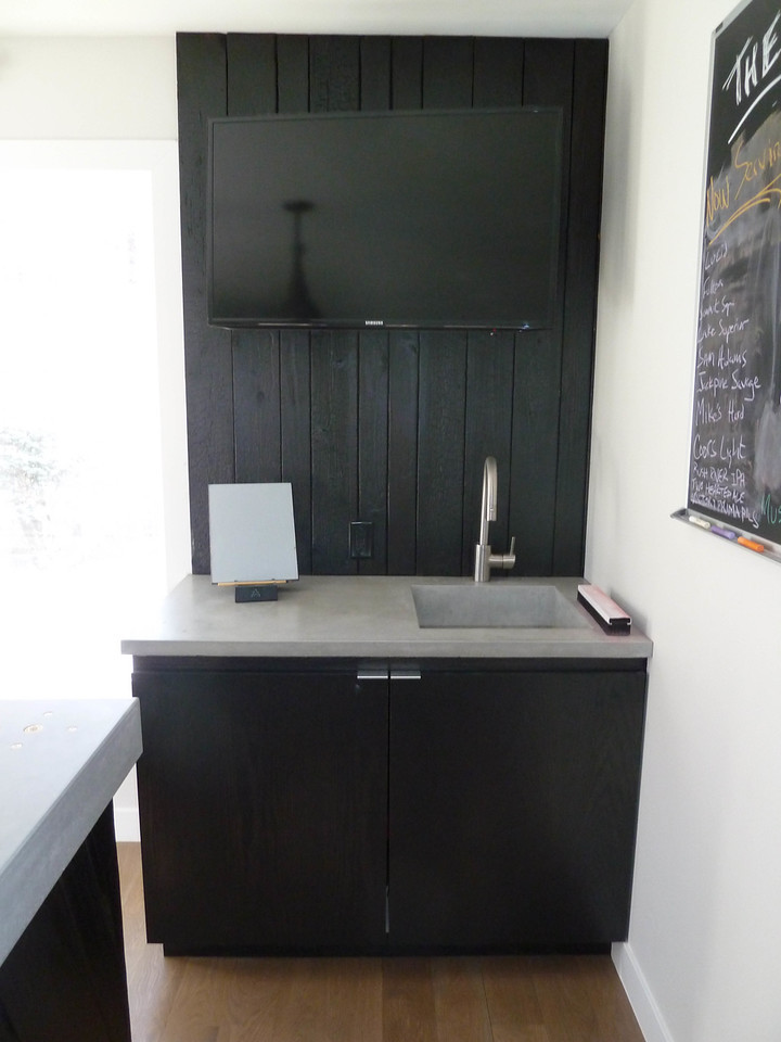 This is an example of a large industrial galley wet bar in Minneapolis with an integrated sink, flat-panel cabinets, dark wood cabinets, concrete benchtops, black splashback and dark hardwood floors.