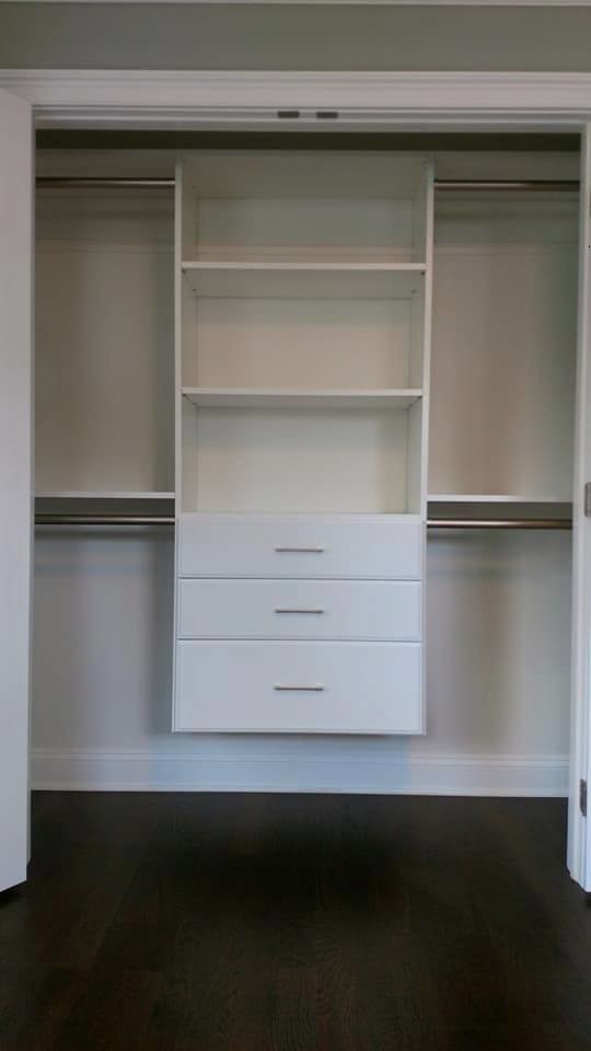 This is an example of a mid-sized modern gender-neutral built-in wardrobe in New York with flat-panel cabinets, white cabinets, dark hardwood floors and brown floor.