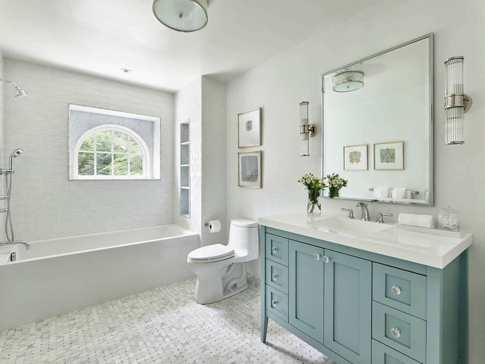 This is an example of a large transitional master bathroom in Philadelphia with shaker cabinets, turquoise cabinets, an alcove tub, a shower/bathtub combo, a one-piece toilet, white tile, porcelain tile, white walls, marble floors, an integrated sink, solid surface benchtops, white floor, an open shower and white benchtops.