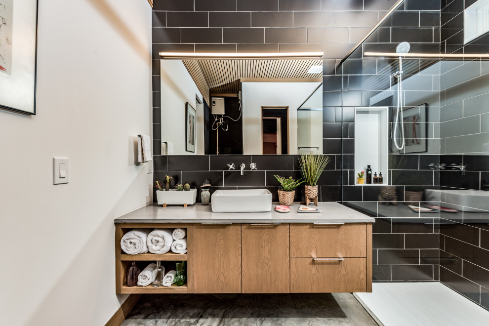 This is an example of a mid-sized eclectic master bathroom in Houston with flat-panel cabinets, light wood cabinets, a curbless shower, a two-piece toilet, black tile, porcelain tile, white walls, concrete floors, a vessel sink, concrete benchtops, grey floor, an open shower, grey benchtops, a laundry, a single vanity, a floating vanity and wood.