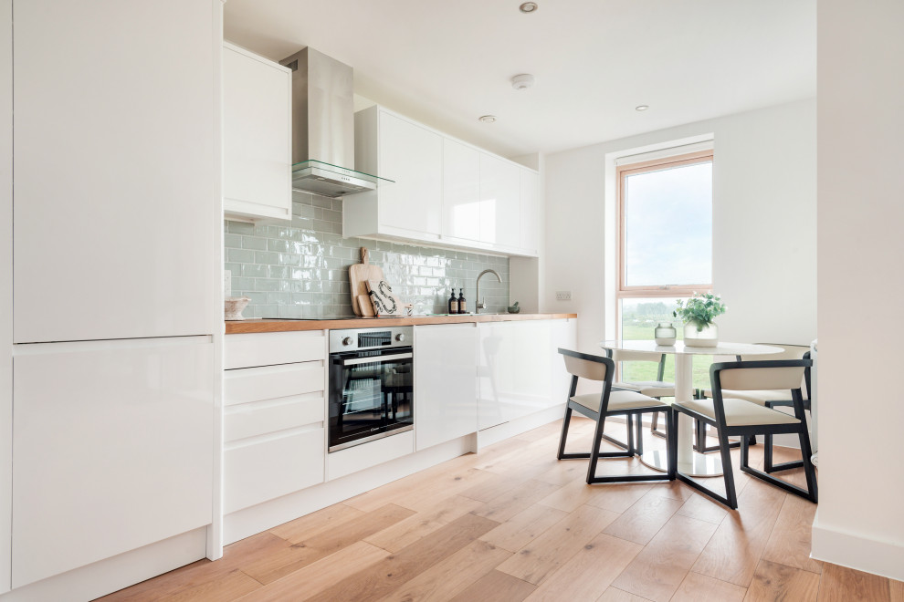 Photo of a contemporary single-wall eat-in kitchen in London with an undermount sink, flat-panel cabinets, white cabinets, wood benchtops, grey splashback, subway tile splashback, panelled appliances, medium hardwood floors, no island, brown floor and brown benchtop.
