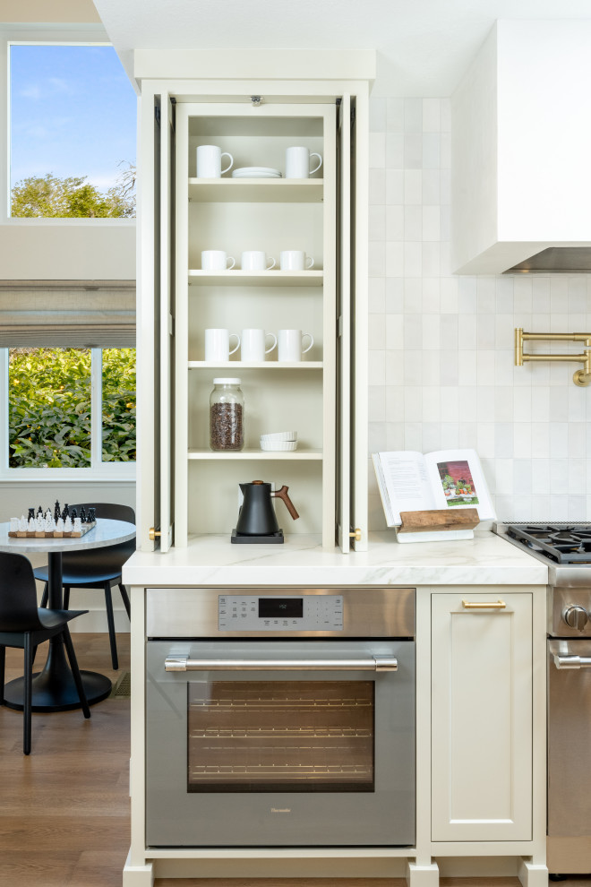 Exempel på ett mellanstort klassiskt vit vitt kök, med en rustik diskho, skåp i shakerstil, beige skåp, bänkskiva i kvarts, vitt stänkskydd, en köksö, brunt golv, stänkskydd i keramik, integrerade vitvaror och laminatgolv