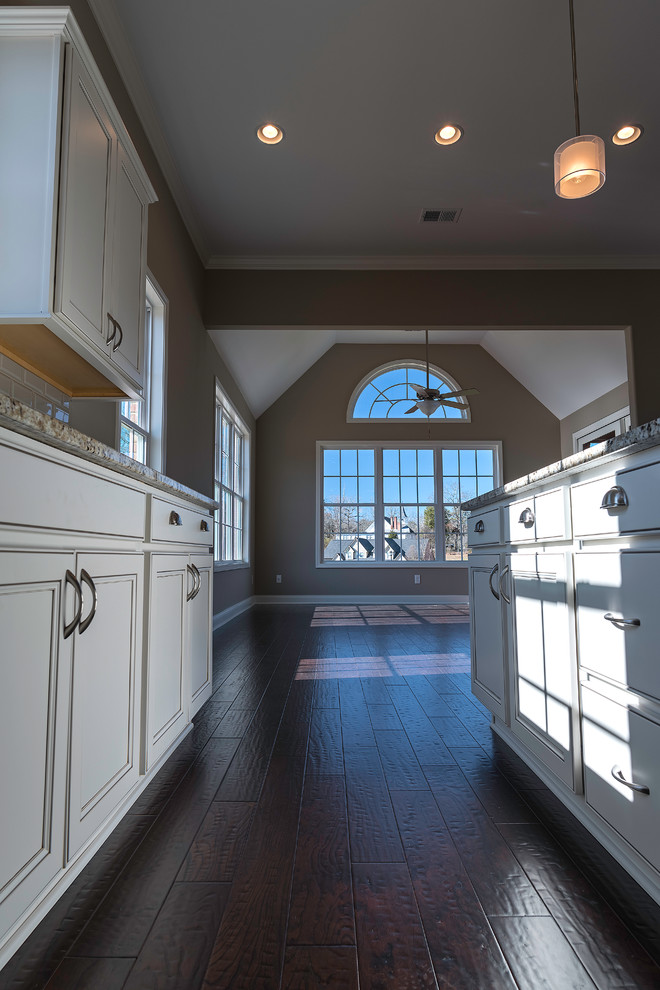 Mid-sized transitional l-shaped dark wood floor open concept kitchen photo with an undermount sink, recessed-panel cabinets, white cabinets, granite countertops, gray backsplash, subway tile backsplash, stainless steel appliances and an island