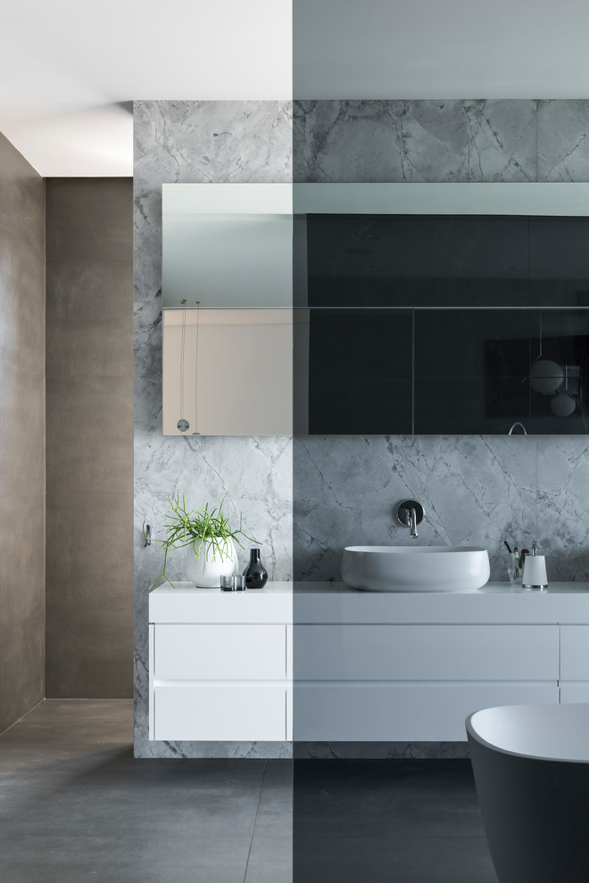 Inspiration for a large modern master bathroom in Sydney with furniture-like cabinets, white cabinets, a freestanding tub, an open shower, a wall-mount toilet, gray tile, marble, grey walls, porcelain floors, a vessel sink, solid surface benchtops, grey floor, an open shower and white benchtops.