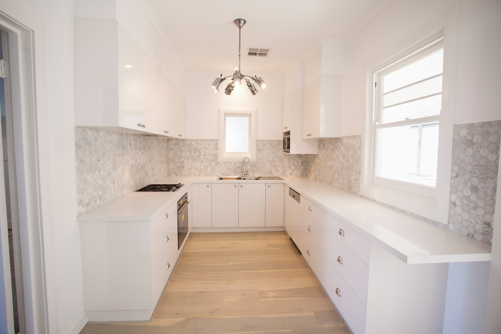 Photo of a beach style u-shaped separate kitchen in Adelaide with a double-bowl sink, flat-panel cabinets, white cabinets, laminate benchtops, grey splashback, white appliances, plywood floors, no island and beige floor.