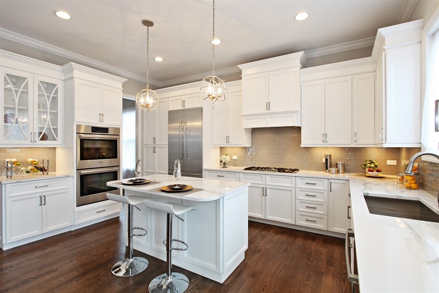 Example of a large transitional l-shaped dark wood floor eat-in kitchen design in Chicago with an undermount sink, shaker cabinets, white cabinets, quartz countertops, beige backsplash, subway tile backsplash, stainless steel appliances and an island